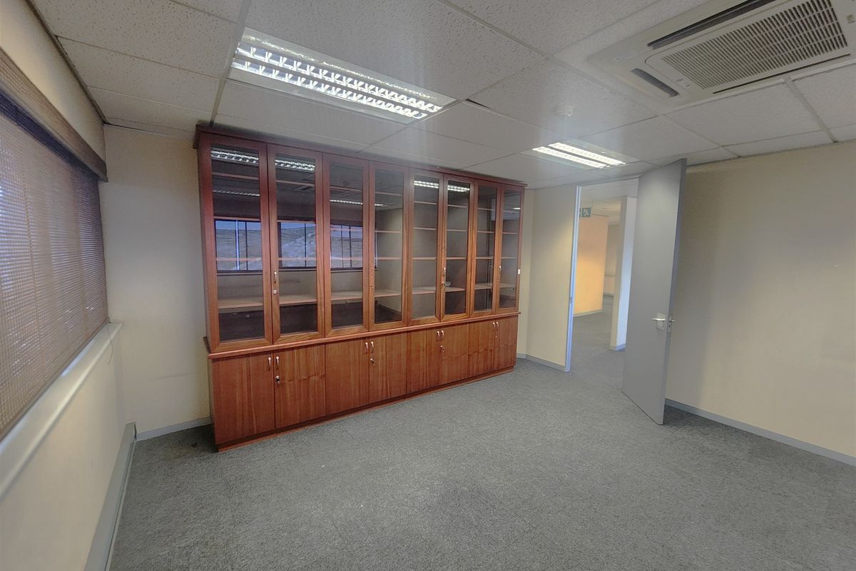 A clean, vacant office space featuring built-in wooden storage cabinetry, carpeted flooring, and integrated ceiling-mounted air conditioning.