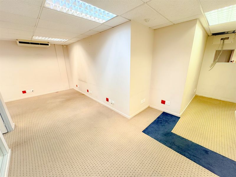 An empty office space featuring suspended ceilings, recessed lighting, wall-mounted air conditioning, and carpeted flooring with multiple electrical and data connection points.