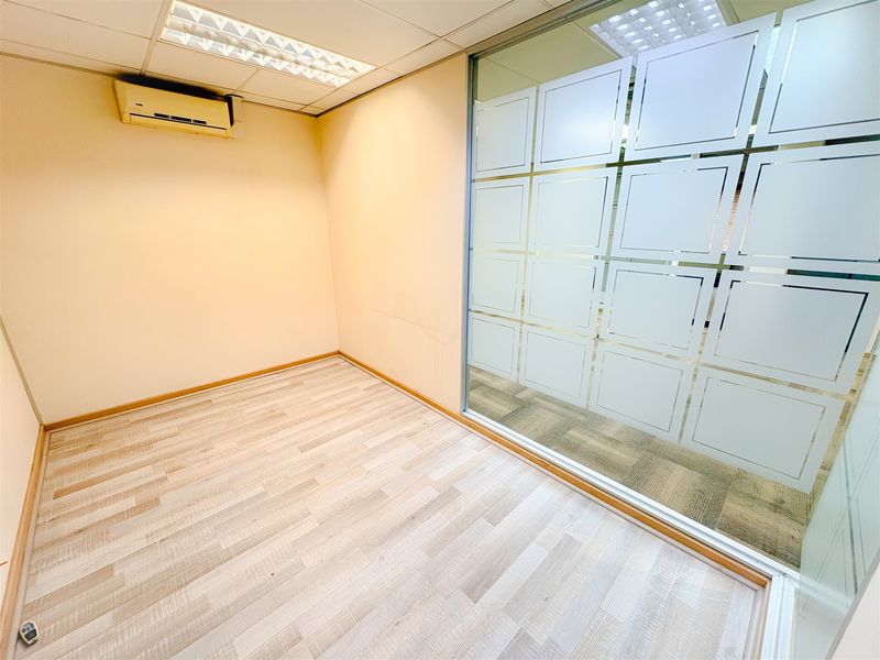 An empty office space featuring a glass partition wall with frosted privacy film, laminate flooring, and a wall-mounted air conditioning unit.
