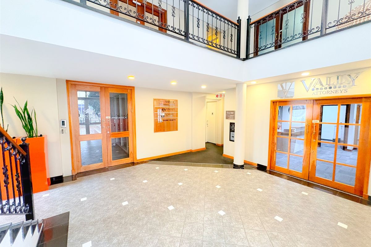Spacious office building entrance lobby featuring tiled flooring, wrought iron balustrades, and multiple wooden-framed glass access doors.