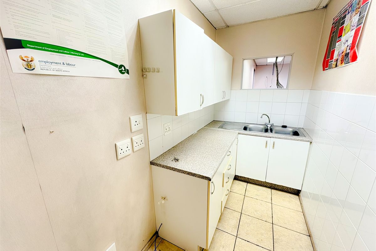 A compact office kitchenette featuring built-in white cabinetry, a stainless steel sink, laminate countertops, and tiled splashbacks in a functional layout.