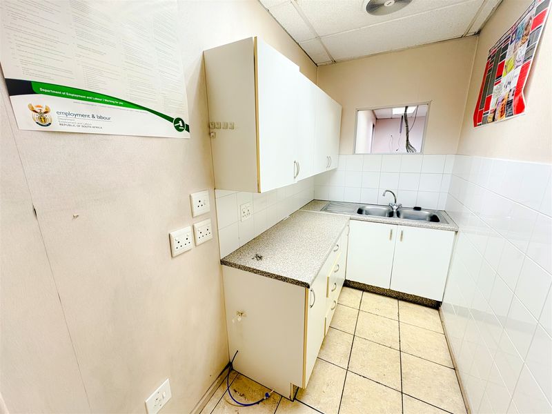 A compact office kitchenette featuring built-in white cabinetry, a stainless steel sink, laminate countertops, and tiled splashbacks in a functional layout.