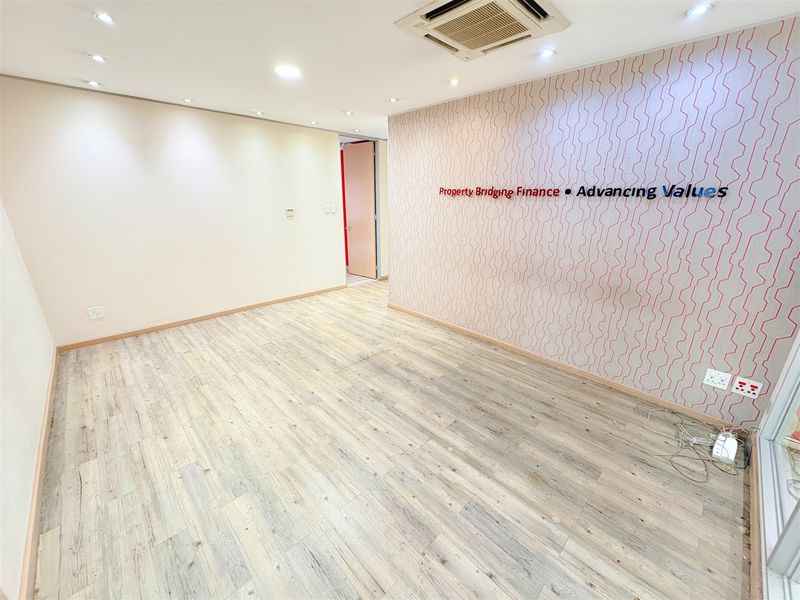 A bright, empty office space featuring modern laminate wood flooring, recessed ceiling lighting, ducted air conditioning, and a decorative feature wall.