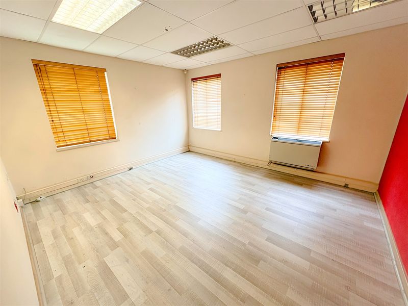 A vacant office space featuring laminate flooring, a suspended ceiling with recessed lighting, and a wall-mounted air conditioning unit.