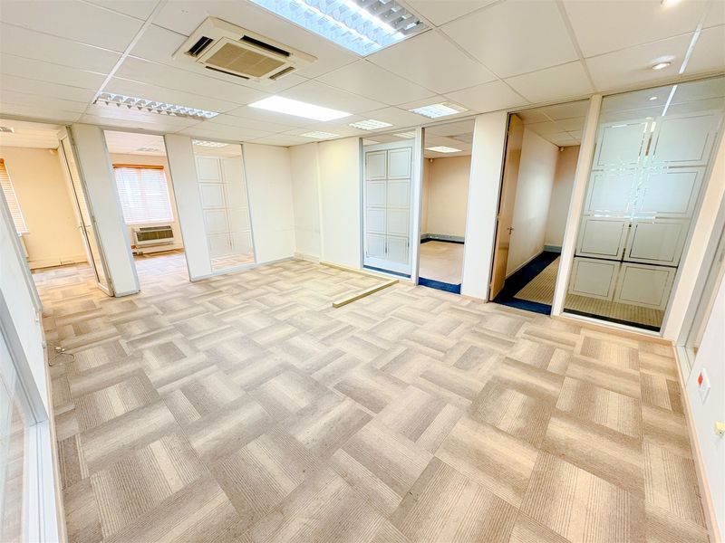 An open-plan office space featuring modular carpet tiles, glass partition walls, and a suspended ceiling with integrated lighting and air conditioning.