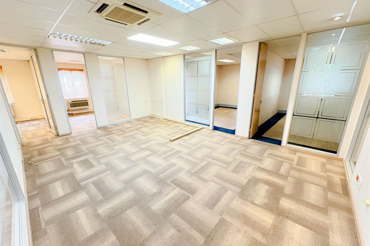 An open-plan office space featuring modular carpet tiles, glass partition walls, and a suspended ceiling with integrated lighting and air conditioning.