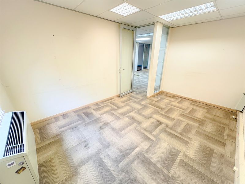 An empty office space featuring carpet tile flooring, a suspended ceiling with recessed lighting, and a glass partition door leading to an adjacent area.