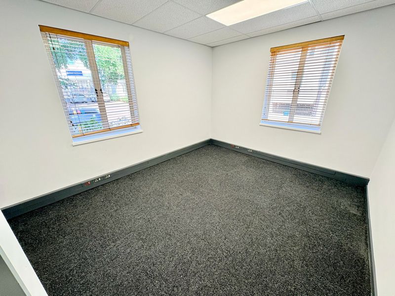 A clean, vacant office space featuring grey carpet flooring, suspended ceiling with recessed lighting, and perimeter trunking for electrical connectivity.