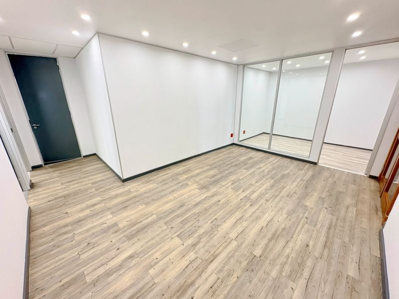 A bright, modern, and empty office space featuring laminate wood flooring, recessed downlighting, and a contemporary glass partition wall.