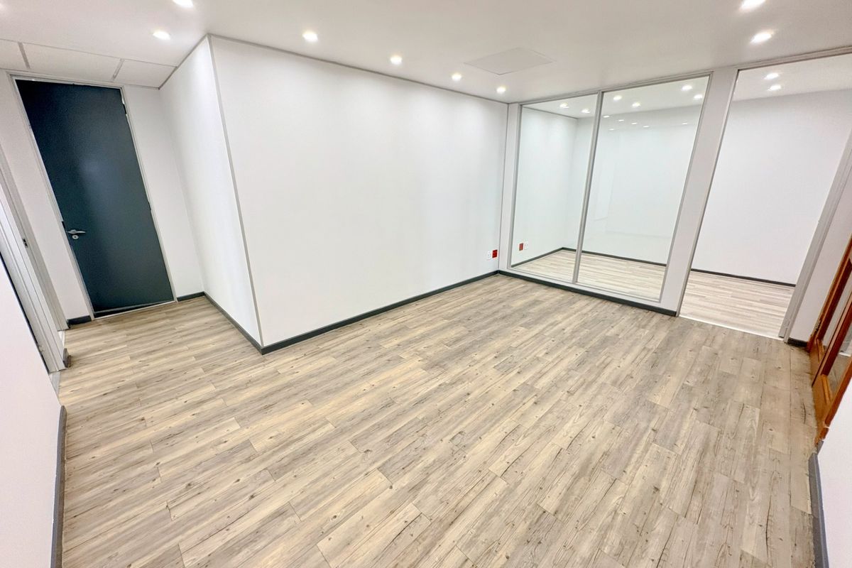 A bright, modern, and empty office space featuring laminate wood flooring, recessed downlighting, and a contemporary glass partition wall.