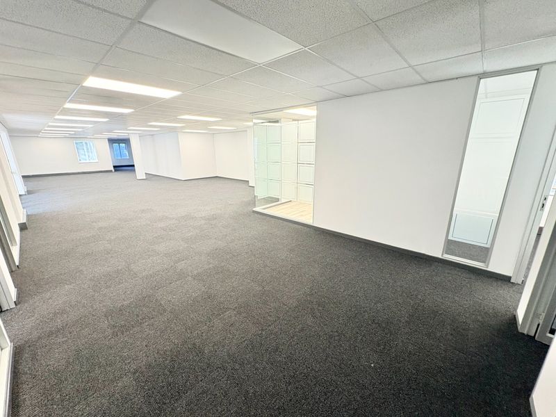 Spacious open-plan office area featuring modern carpet tiles, a suspended ceiling with recessed lighting, and a glass-partitioned meeting room.
