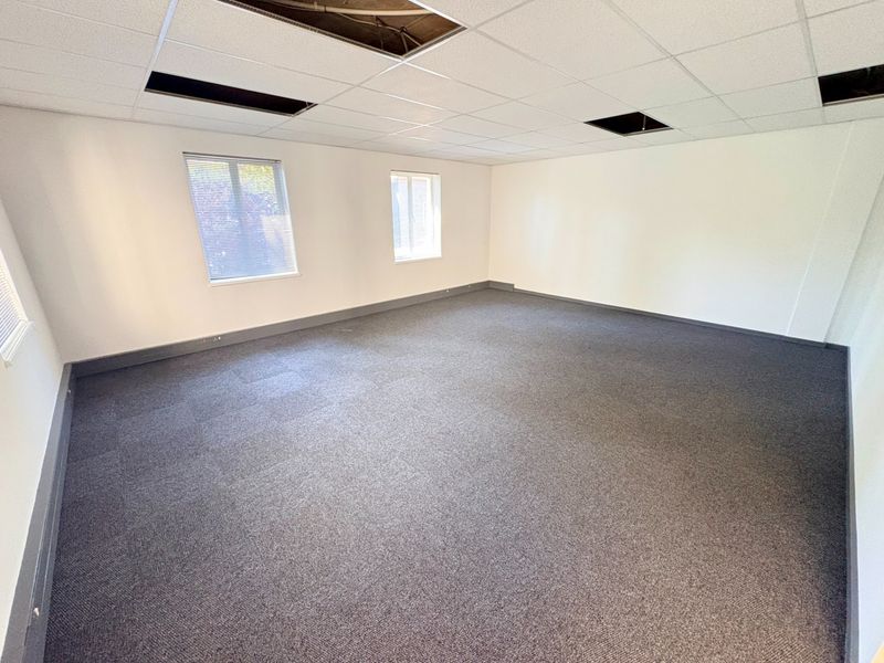 An empty office space featuring carpet tiles, venetian blinds, and a suspended ceiling with several missing tiles requiring repair.