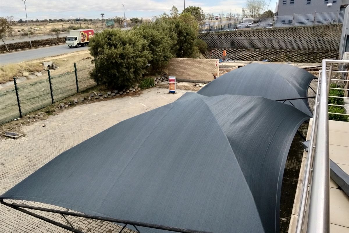 Elevated view of an industrial parking area featuring large shade cloth carports, paved surfacing, and perimeter security fencing.