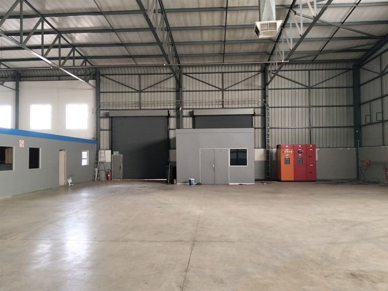 Spacious industrial warehouse featuring high ceilings with exposed steel trusses, concrete flooring, roller shutter access, and integrated electrical distribution panels.