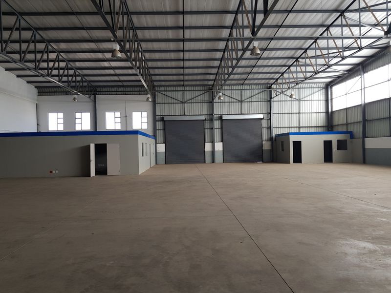 Spacious industrial warehouse featuring high-clearance steel truss roofing, concrete flooring, multiple roller shutter doors, and integrated internal office structures.