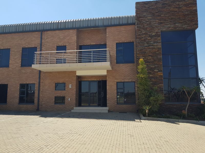 Modern industrial office building featuring a face brick facade, stone cladding accents, a balcony with stainless steel railings, and a paved parking area.