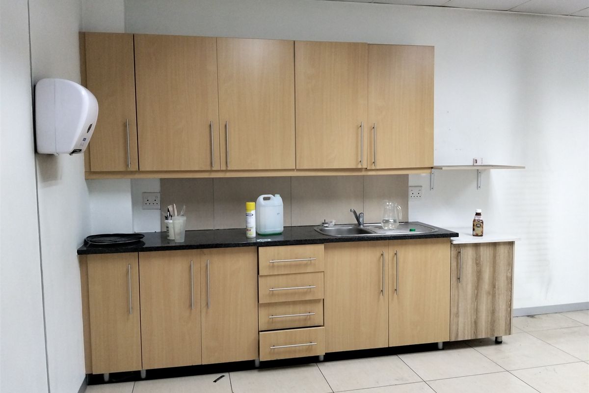 A functional kitchenette area featuring light wood-finish cabinetry, a stainless steel sink, and tiled flooring, suitable for office or industrial utility use.