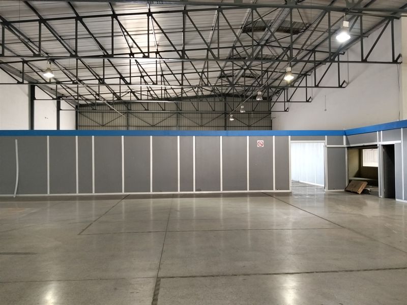 Spacious industrial warehouse area featuring high exposed steel roof trusses, polished concrete flooring, and partitioned office sections, suitable for various commercial or storage uses.