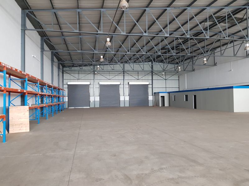 Spacious industrial warehouse featuring high steel truss ceilings, concrete flooring, multiple roller shutter doors, and integrated metal racking for efficient storage and logistics operations.
