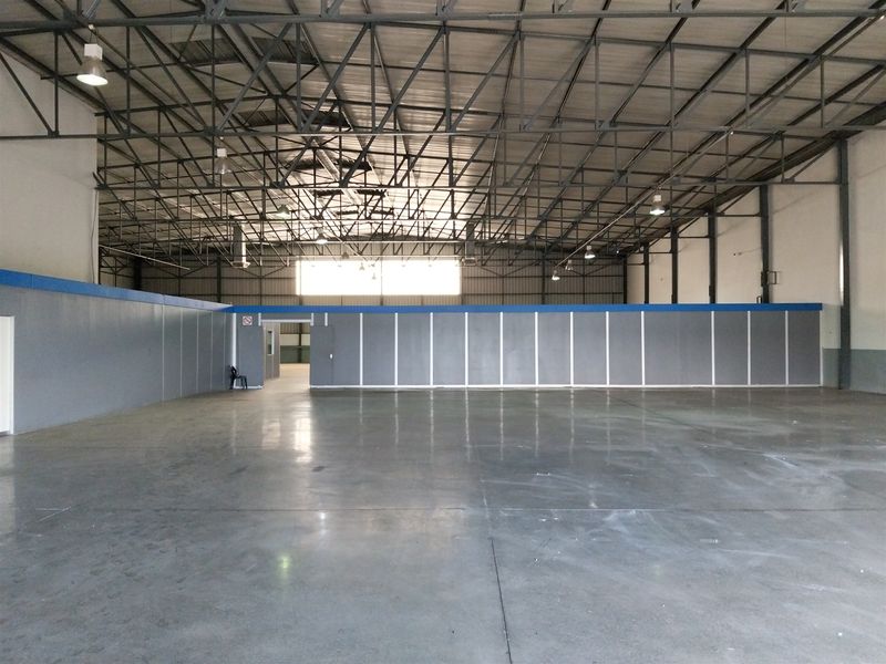 Spacious industrial warehouse featuring high exposed steel roof trusses, polished concrete flooring, and a partitioned office area with integrated lighting.