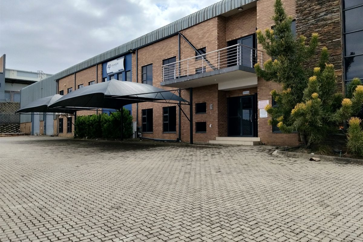 Front exterior view of an industrial property featuring a brick facade, paved driveway, shade cloth carport, and a balcony with metal railing.