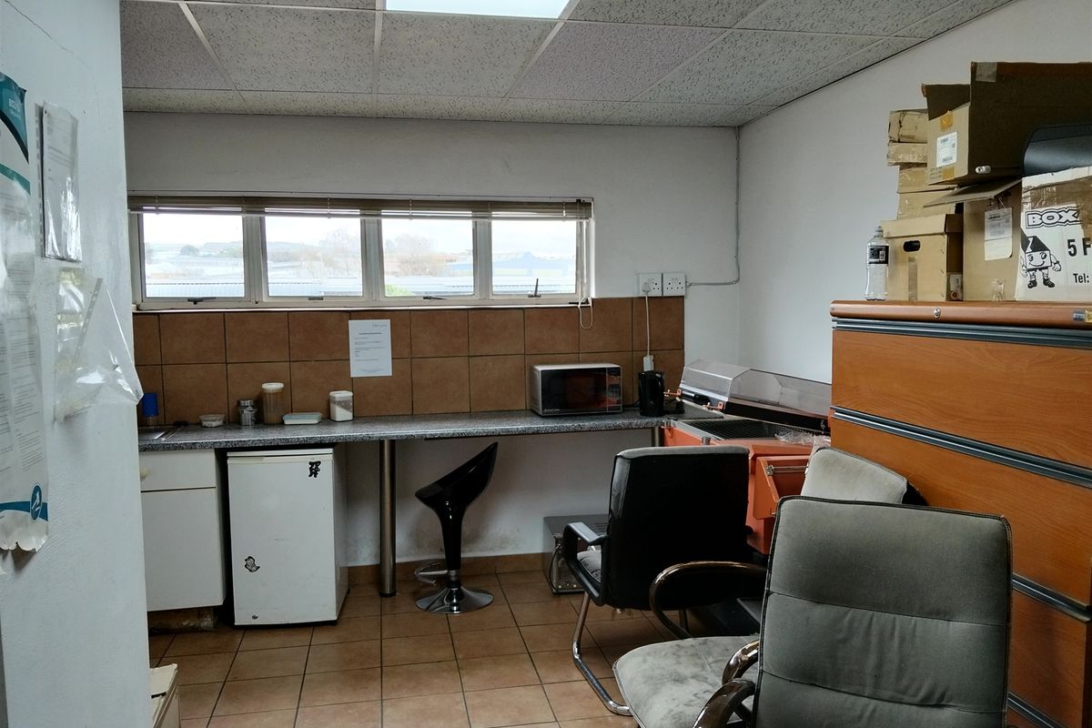 A functional industrial kitchenette featuring tiled flooring, a laminate countertop, tiled backsplash, and a drop ceiling with integrated lighting.