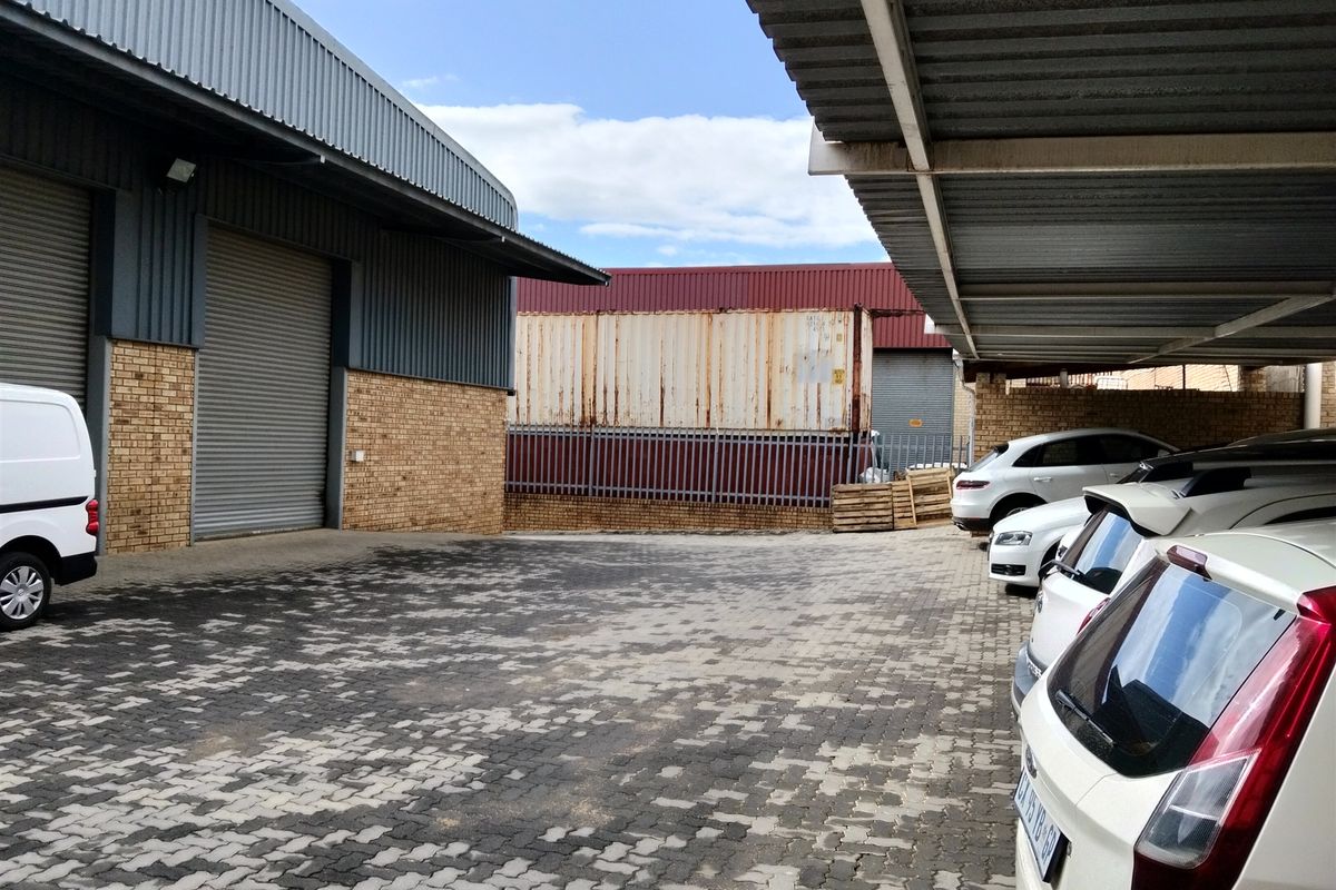 Industrial yard area featuring a large roller shutter door, brick facade, and covered parking structure with paved surfacing.