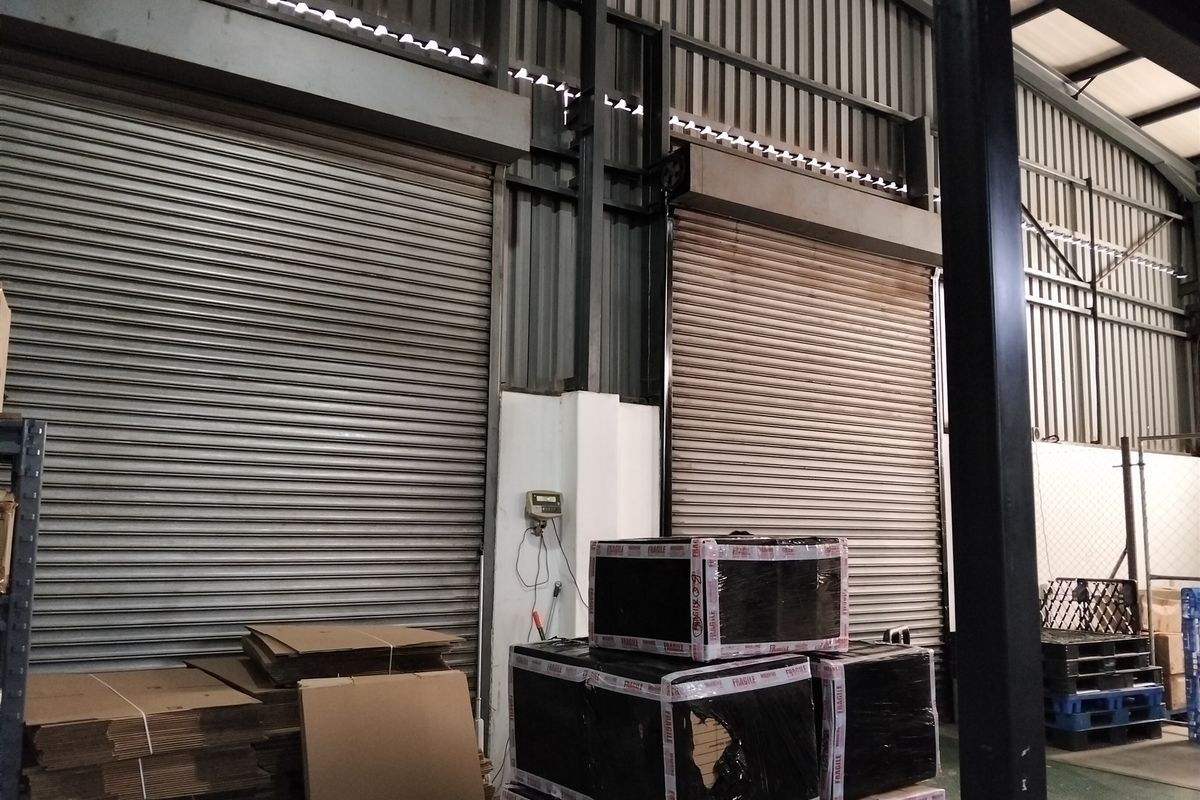 Industrial warehouse interior featuring high ceilings, exposed steel structural elements, and multiple large roller shutter doors for loading access.