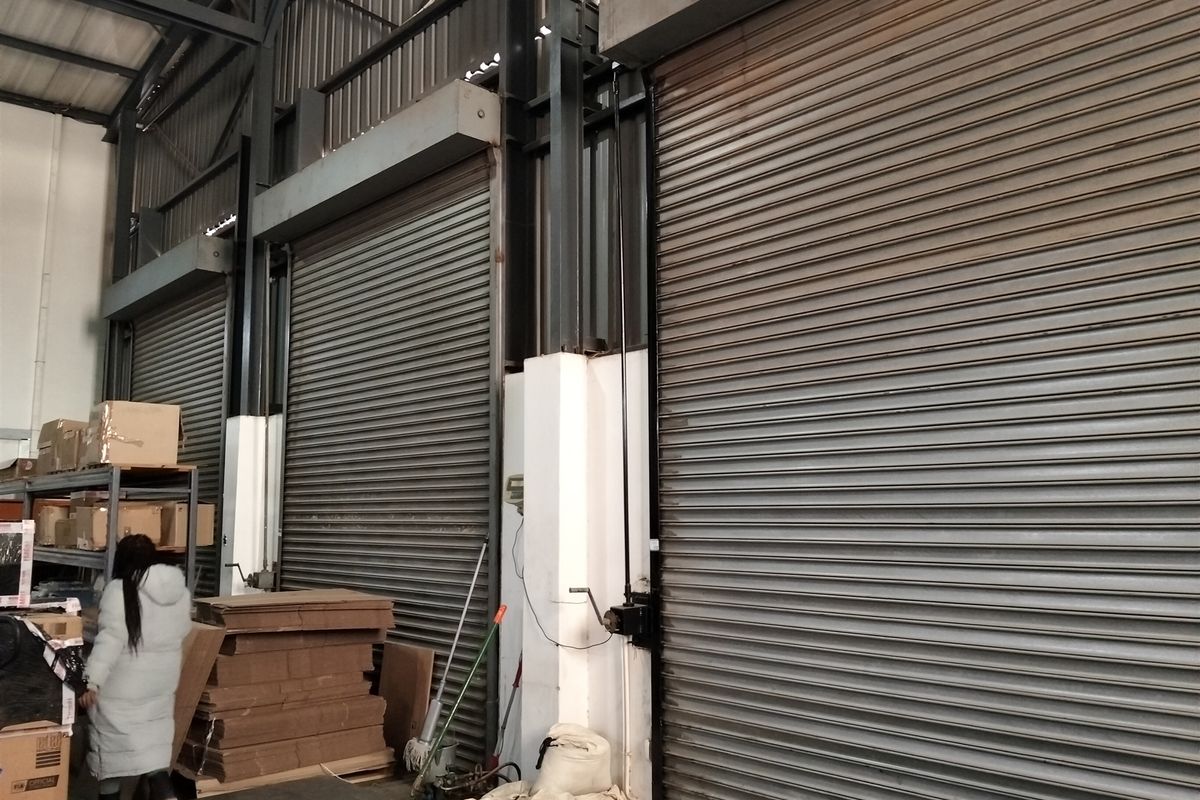 Industrial warehouse space featuring high ceilings with exposed steel trusses and multiple large roller shutter doors for efficient loading and access.