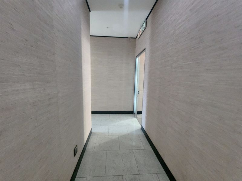 A clean, well-maintained office hallway featuring neutral textured wall finishes, tiled flooring, and a clear emergency exit sign.
