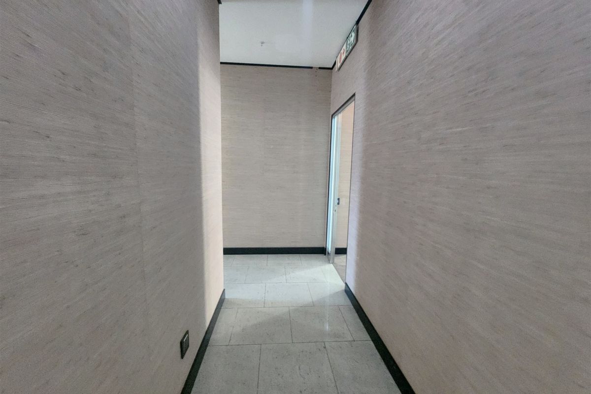 A clean, well-maintained office hallway featuring neutral textured wall finishes, tiled flooring, and a clear emergency exit sign.