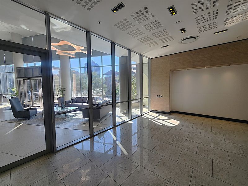 Modern office lobby or reception area featuring polished tile floors, glass partitioning, and contemporary recessed ceiling lighting with a view into an adjacent lounge.