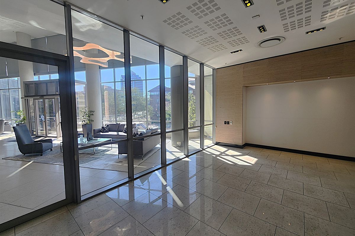 Modern office lobby or reception area featuring polished tile floors, glass partitioning, and contemporary recessed ceiling lighting with a view into an adjacent lounge.