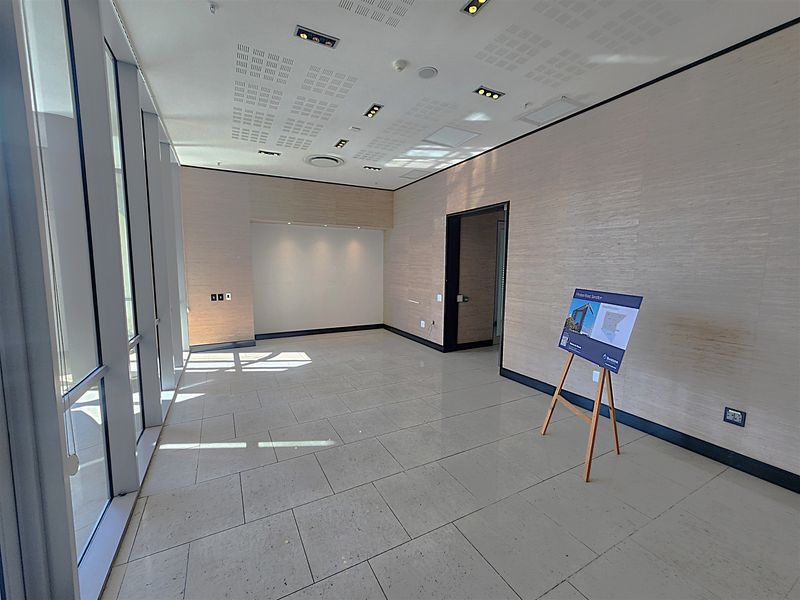 A bright, modern, and vacant office space featuring large floor-to-ceiling windows, tiled flooring, and recessed ceiling lighting, ideal for a professional workspace.