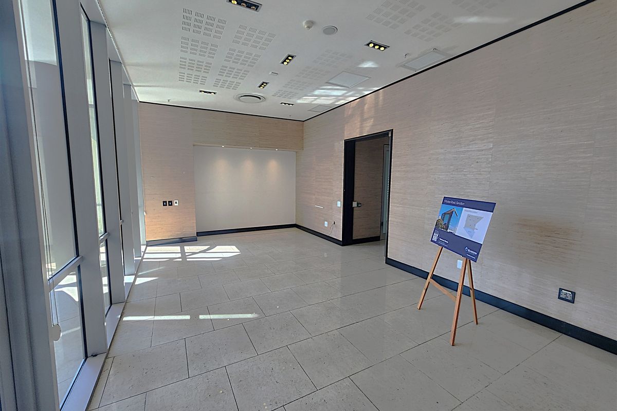 A bright, modern, and vacant office space featuring large floor-to-ceiling windows, tiled flooring, and recessed ceiling lighting, ideal for a professional workspace.