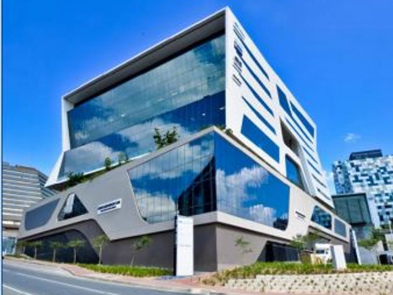 A modern multi-story office building featuring a striking glass curtain wall facade and contemporary architectural design, situated on a prominent street corner.