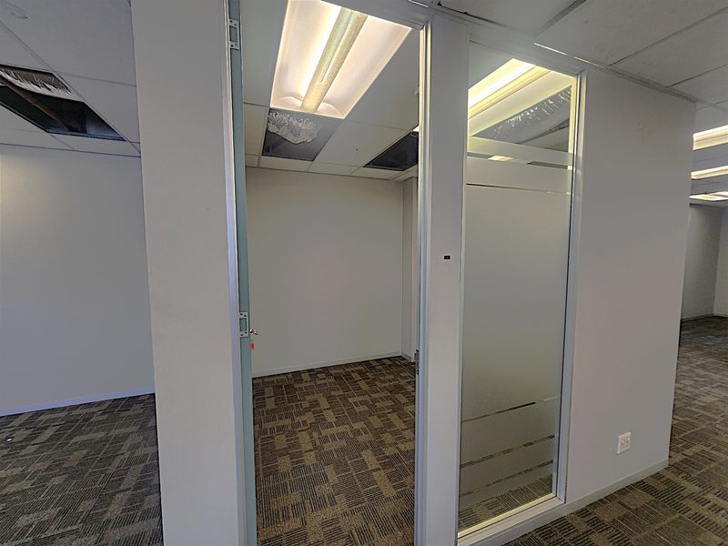 Empty office space featuring glass partitioning, carpet tiles, and a suspended ceiling with damaged and missing tiles.