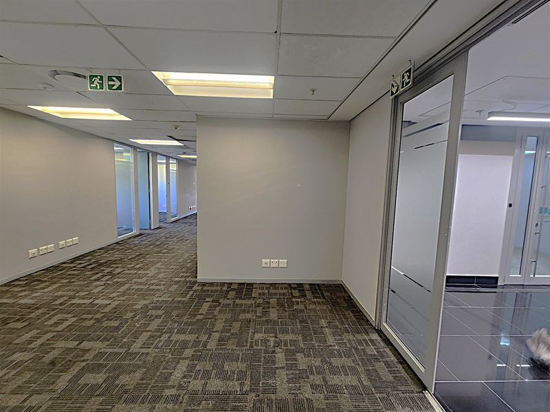 A modern, vacant office space featuring carpeted flooring, suspended ceilings with recessed lighting, and glass partition walls for a professional, open-plan layout.