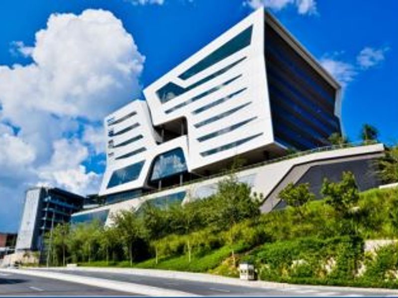 A striking modern office building featuring a contemporary white facade with extensive glass elements, situated above a landscaped embankment.