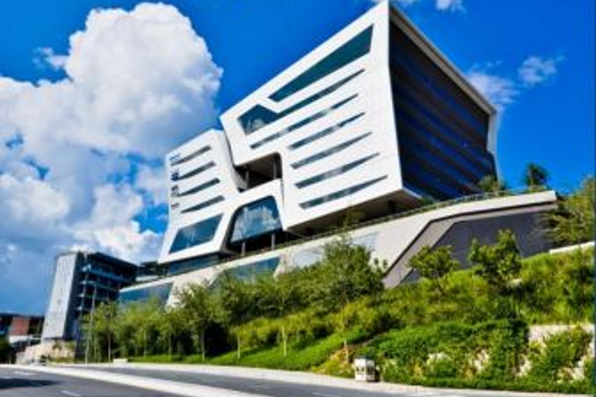 A striking modern office building featuring a contemporary white facade with extensive glass elements, situated above a landscaped embankment.