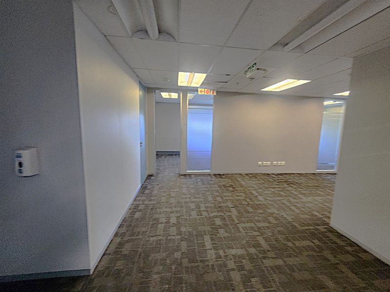 An open-plan office space featuring carpet tiles, suspended ceilings with recessed lighting, and glass partition walls, providing a clean and functional professional environment.