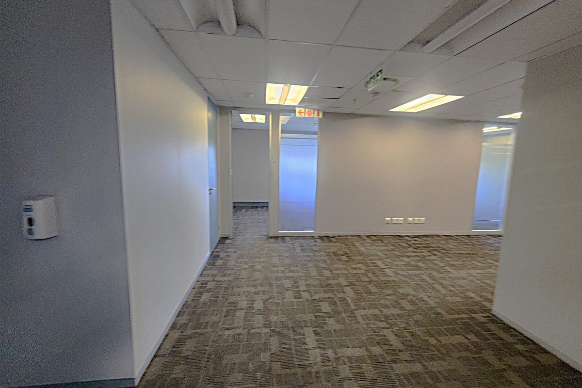 An open-plan office space featuring carpet tiles, suspended ceilings with recessed lighting, and glass partition walls, providing a clean and functional professional environment.