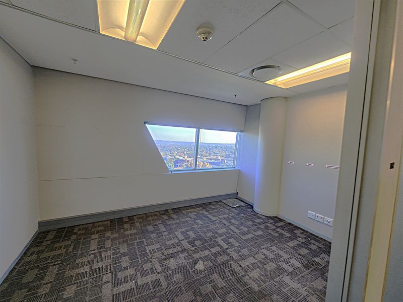 An empty office space featuring carpet tiles, recessed lighting, and a large window with an expansive city view.