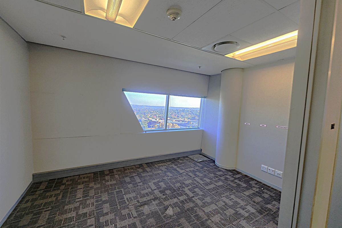 An empty office space featuring carpet tiles, recessed lighting, and a large window with an expansive city view.