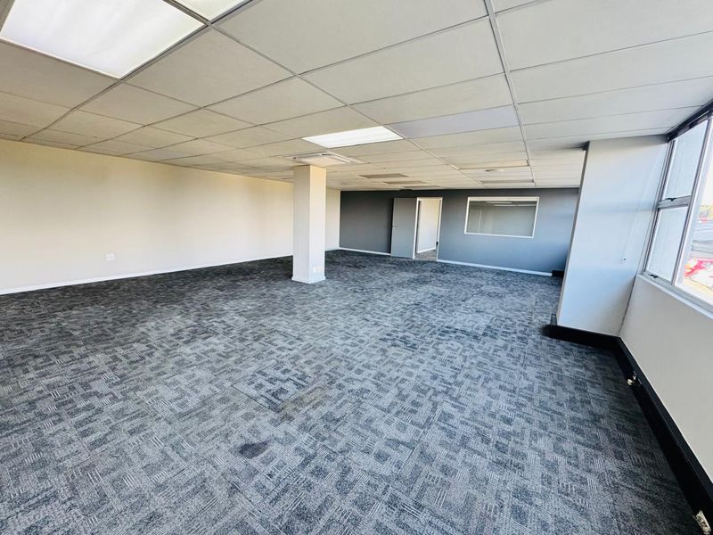 Spacious open-plan office area featuring a suspended ceiling, recessed lighting, and durable carpet tiles, offering a versatile workspace layout.