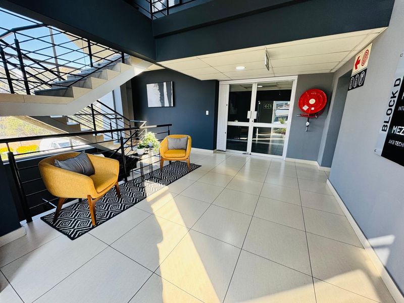 Modern office building entrance lobby featuring tiled flooring, a prominent staircase with metal balustrades, and a wall-mounted fire hose reel.