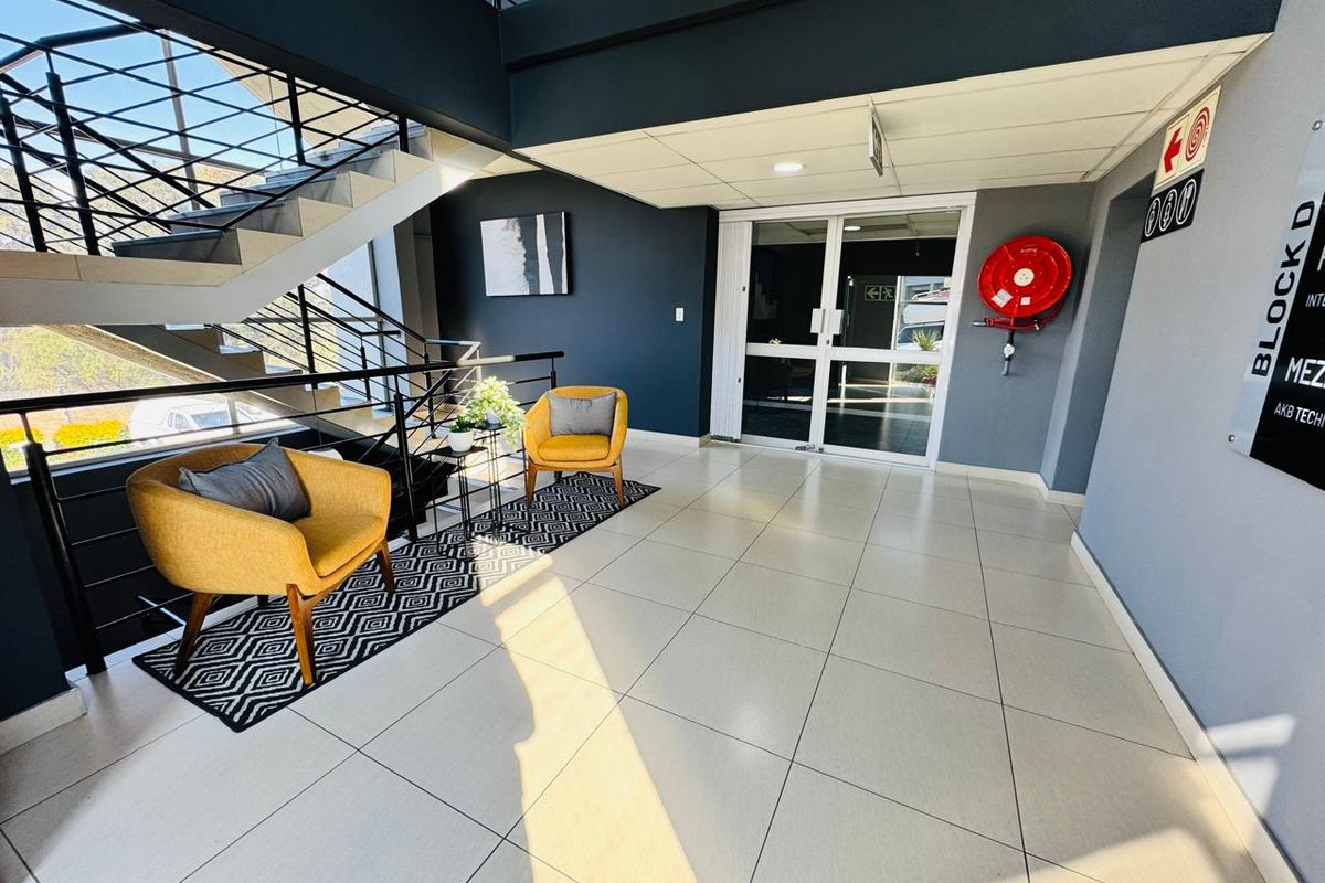 Modern office building entrance lobby featuring tiled flooring, a prominent staircase with metal balustrades, and a wall-mounted fire hose reel.