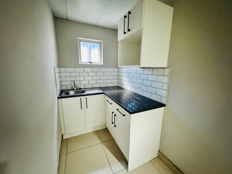 A compact, modern kitchenette featuring white cabinetry, a black granite countertop, subway tile backsplash, and a stainless steel sink.
