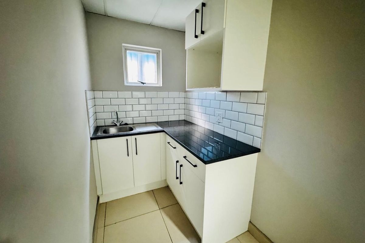 A compact, modern kitchenette featuring white cabinetry, a black granite countertop, subway tile backsplash, and a stainless steel sink.