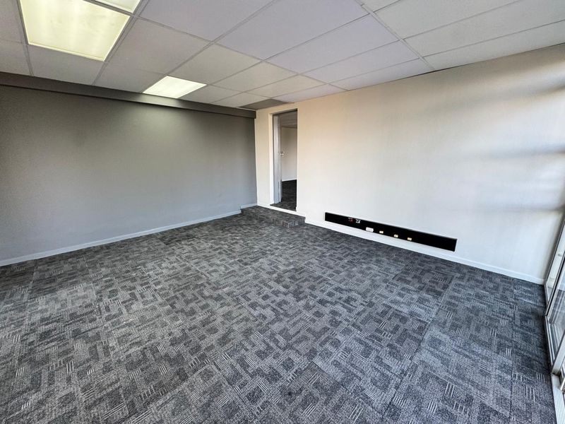 A clean, vacant office space featuring modern carpet tiles, a suspended ceiling with recessed lighting, and integrated electrical trunking along the wall.